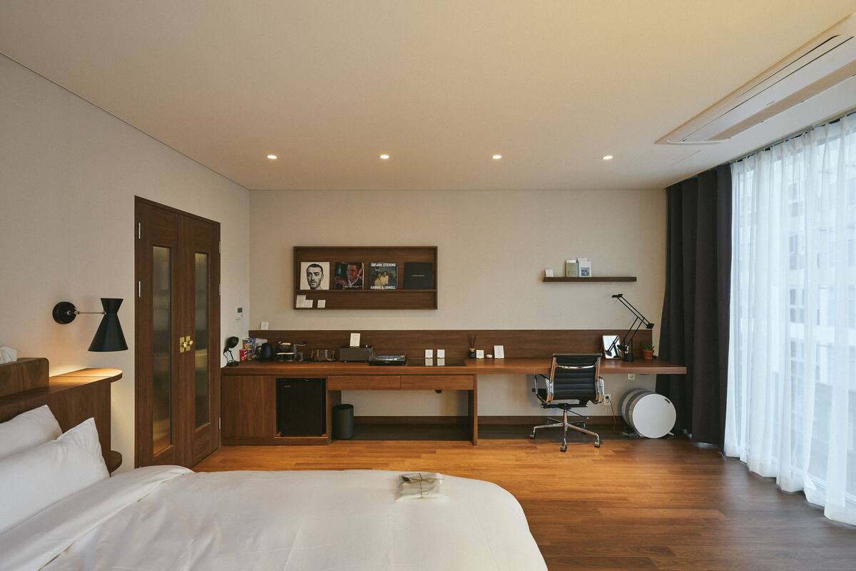 A hotel room with a bed, desk, chair, and a small kitchenette area.