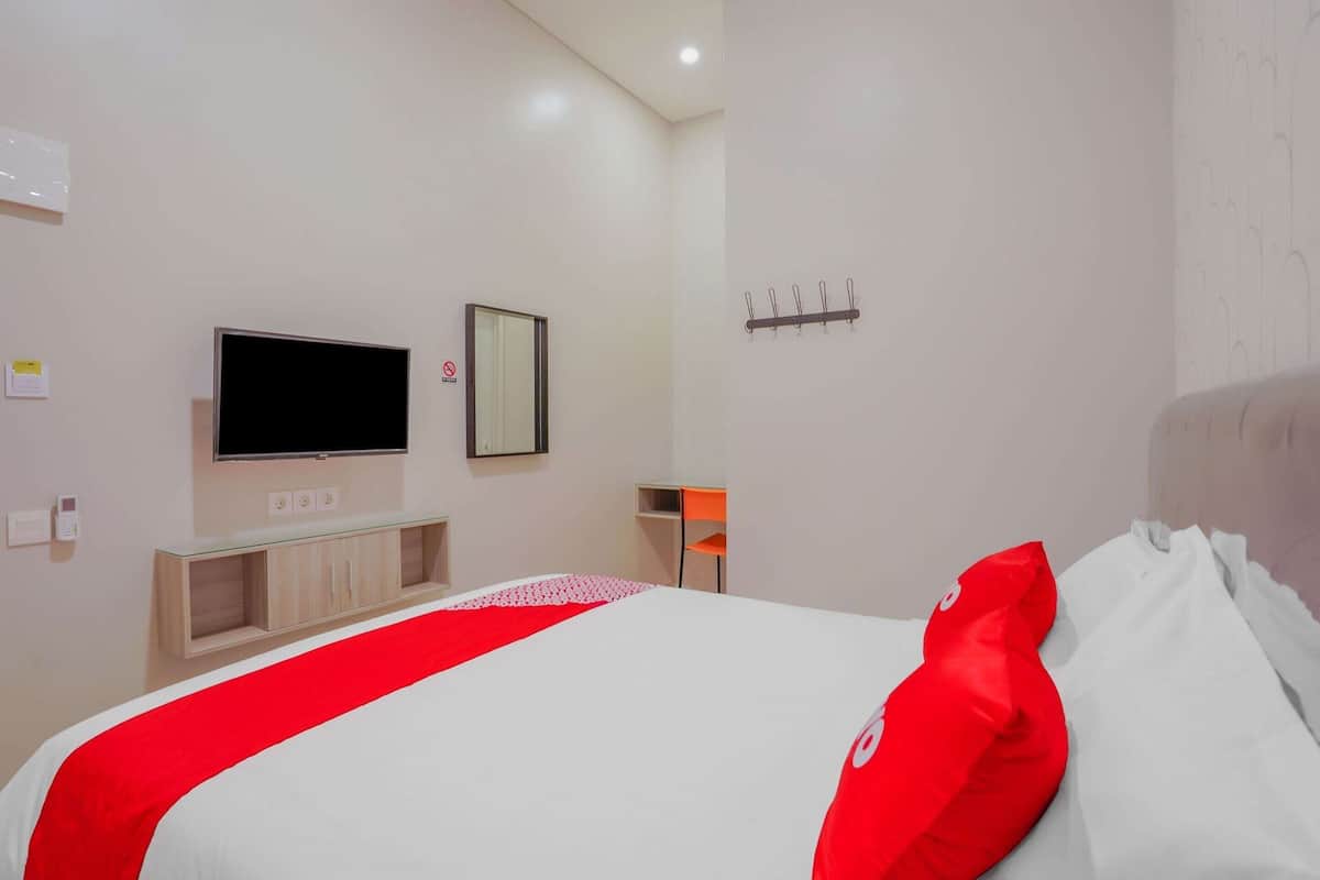 Habitación de hotel con cama, televisor montado en la pared, una mesita y una silla.