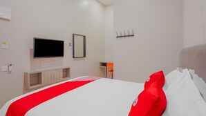 Ein Hotelzimmer mit Bett, Fernseher, Spiegel, Kleiderhaken und einem kleinen Tisch mit Stuhl.