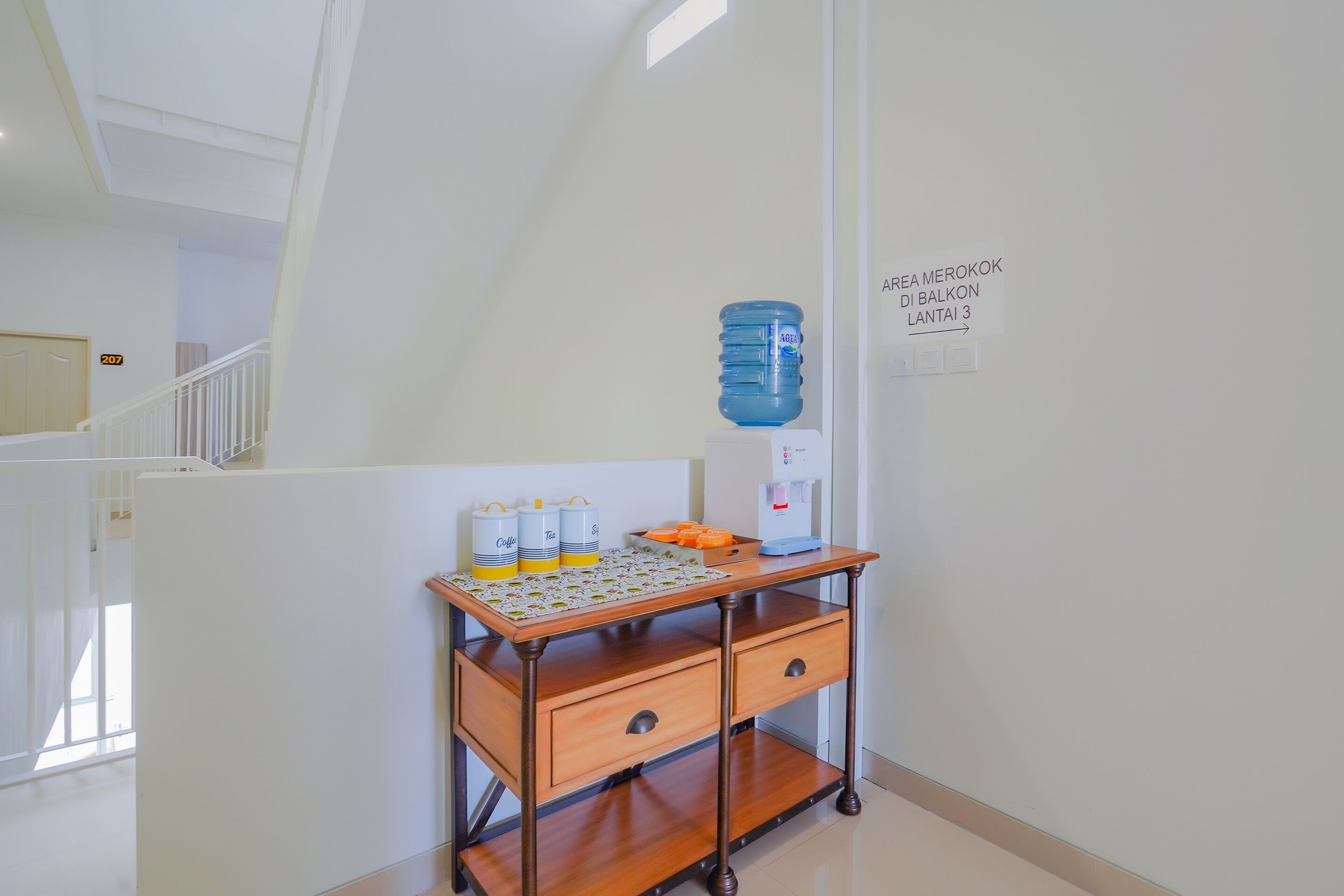 A hotel room with a wooden cart containing a water dispenser, a coffee maker, and a tray of orange slices.