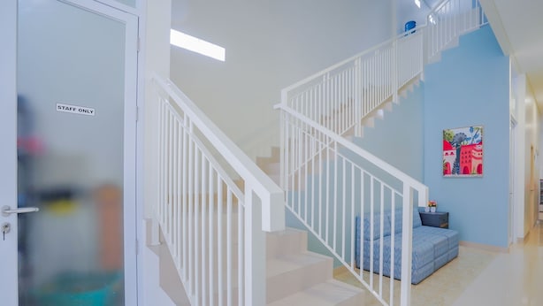 Ein Hotelgang mit einer Tür mit der Aufschrift 'STAFF ONLY', einer Treppe mit weißen Geländern und einer blauen Wand mit einem farbenfrohen Gemälde.