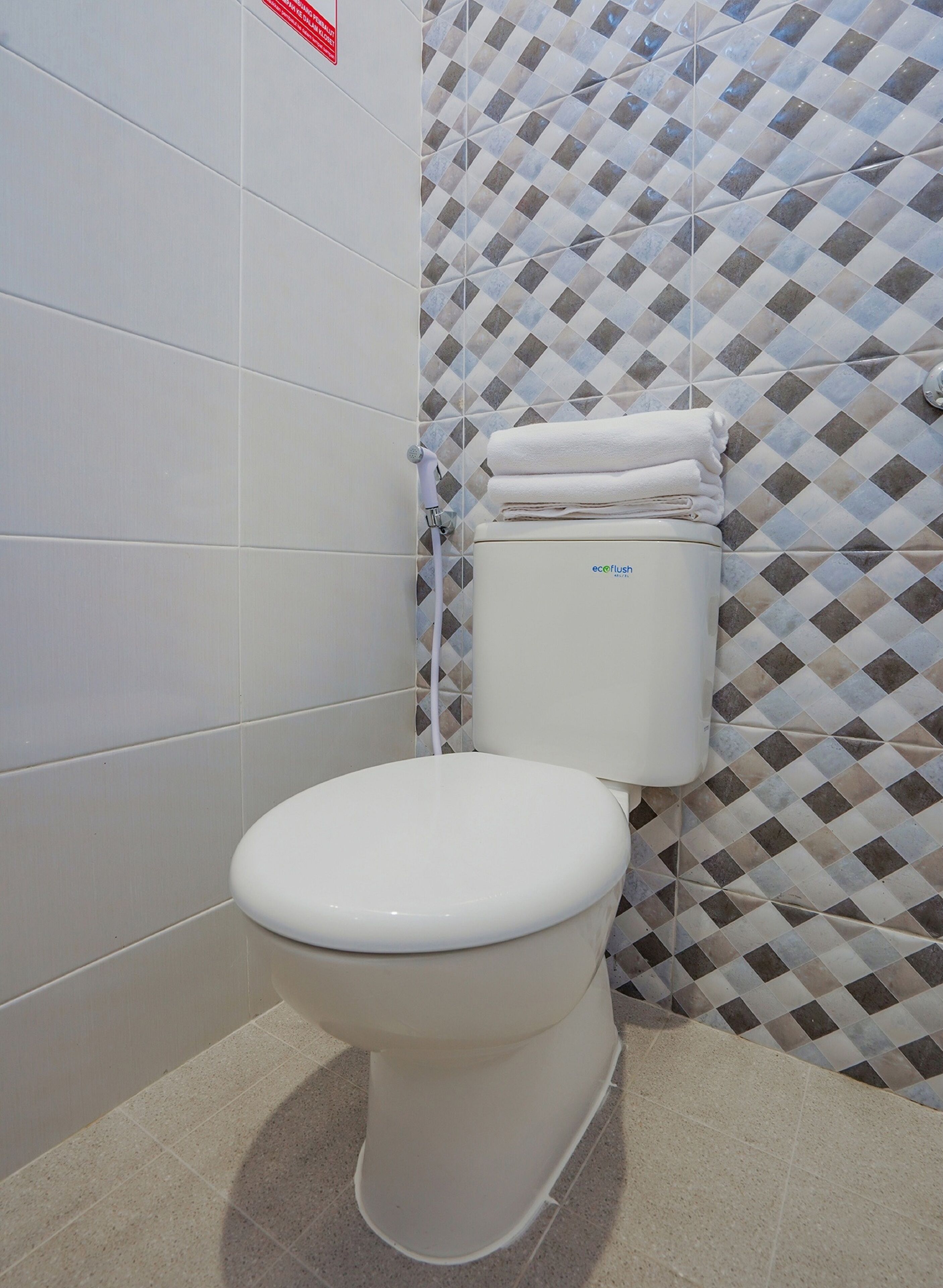 A toilet with a white tank and lid, a white towel stacked on top, and a patterned wall behind it.