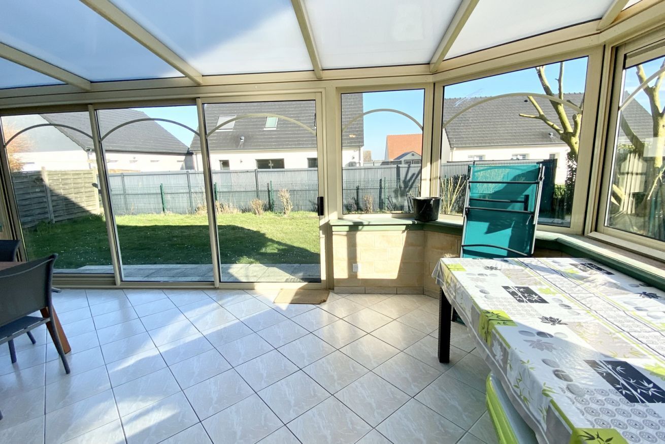 Un invernadero con puerta corredera de vidrio que da a un patio trasero, una mesa de comedor y una silla.