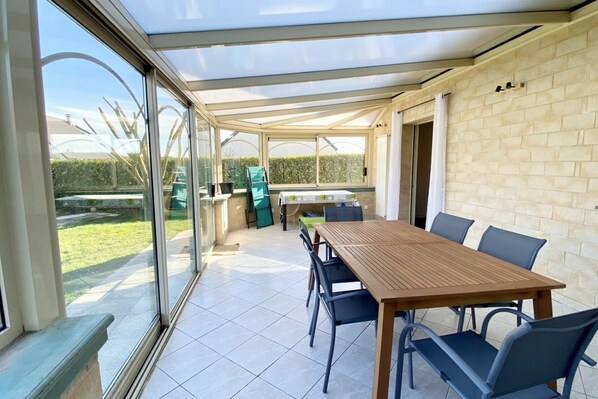 A covered patio area with a table and chairs, a glass door leading outside, and a brick wall.