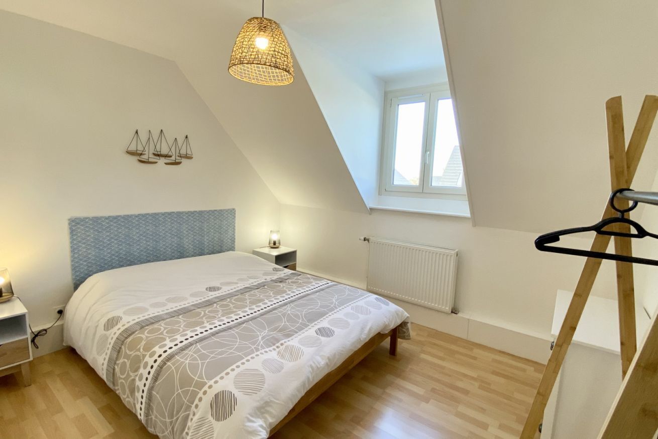 Une chambre avec un plafond en pente, un lit recouvert d’une couvre-lit à motifs, des lampes de chevet, un radiateur et une fenêtre.