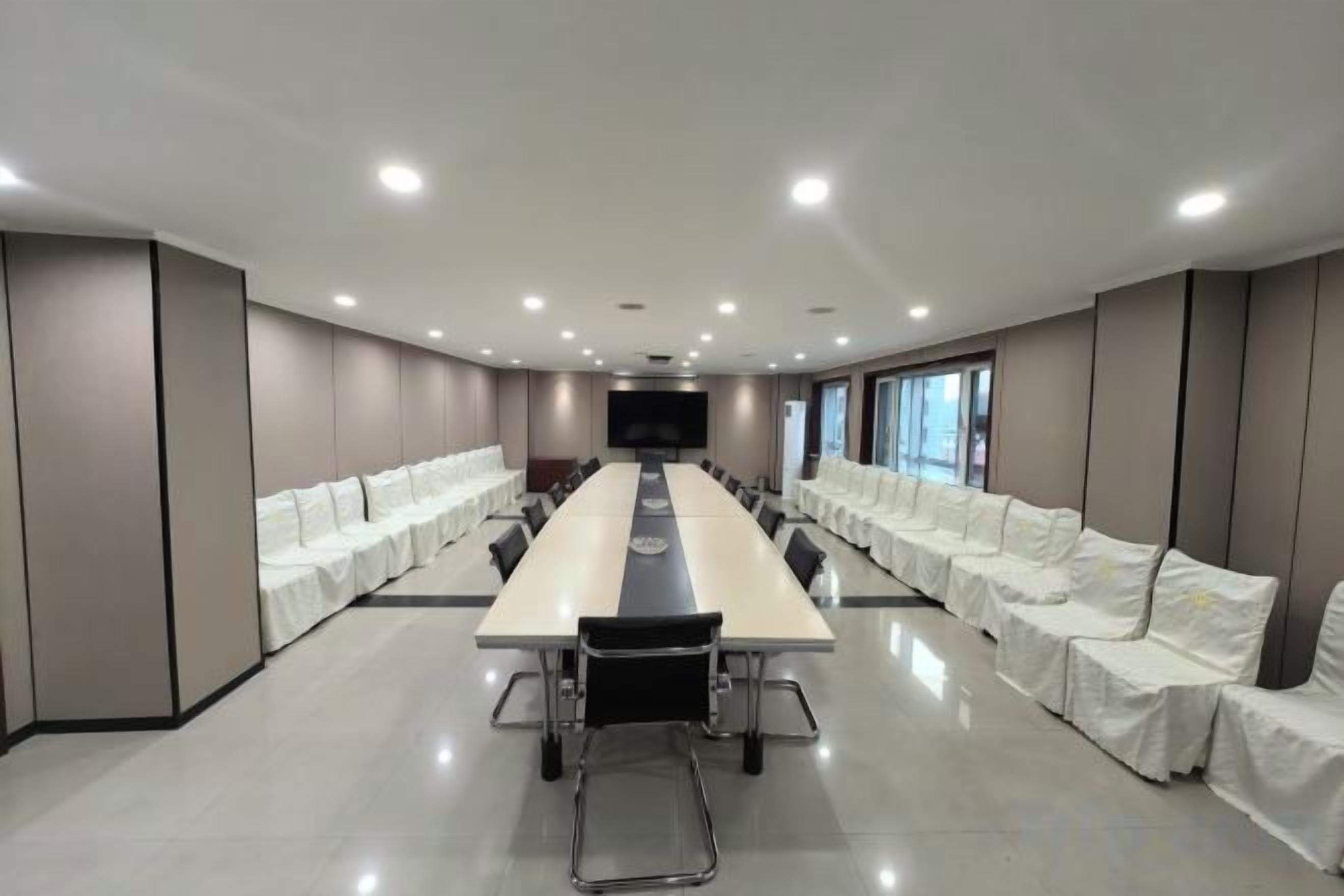 A conference room with a long table, chairs, and white-covered seating on both sides.