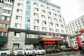 A multi-story hotel with a prominent entrance, several parked cars, and a clear view of the building's facade. - Tianhe Hotel (Huinan)