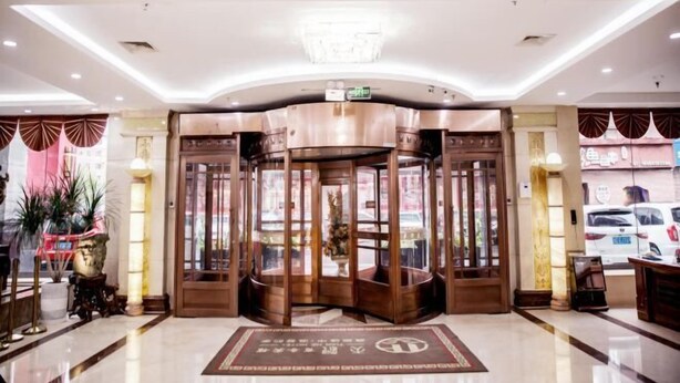 Un vestíbulo de hotel con una puerta giratoria, un candelabro y un mostrador de recepción.