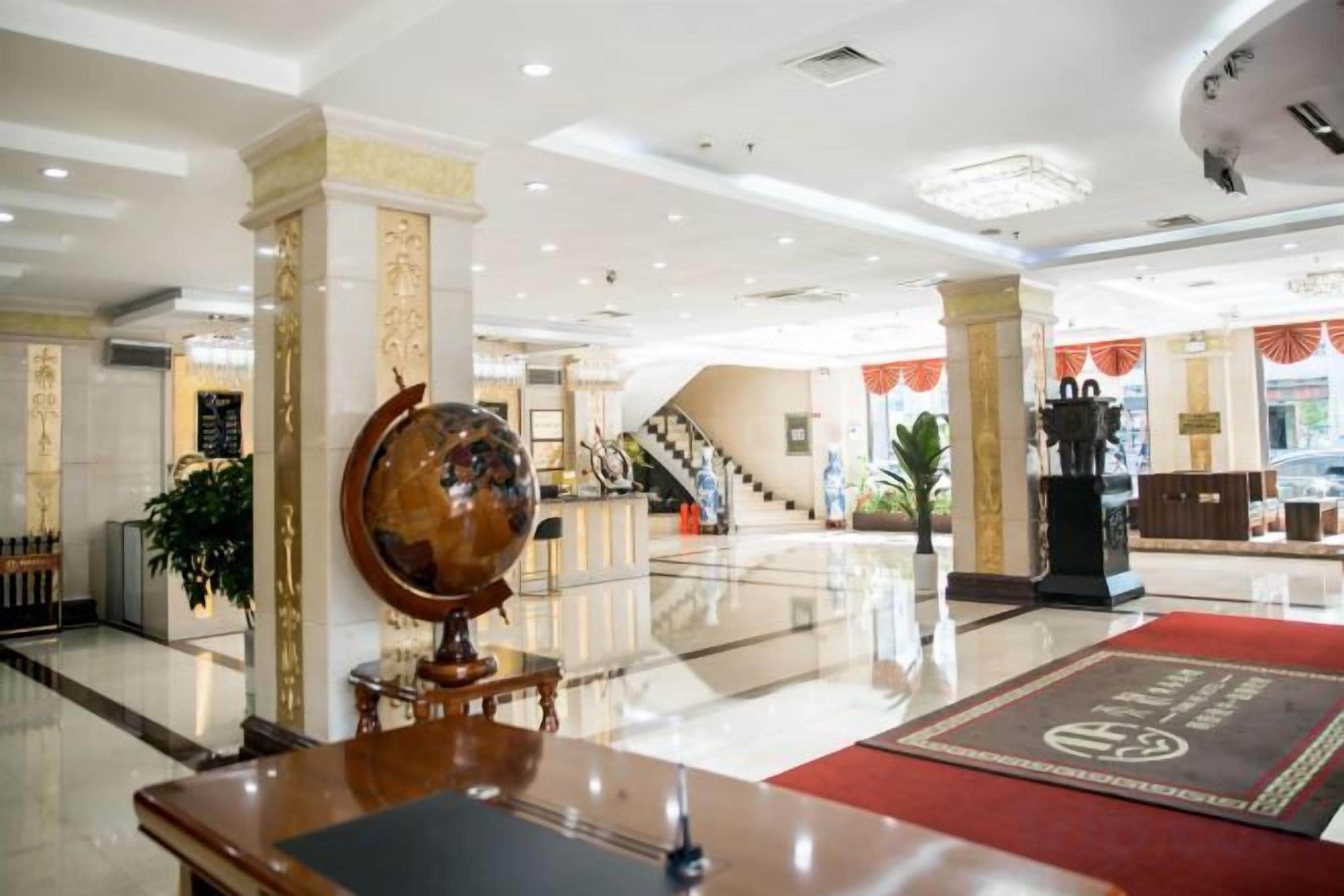 A hotel lobby with a reception desk, a globe, and a staircase in the background.