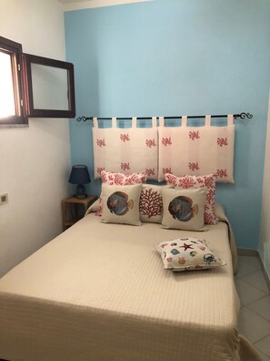 A bedroom with a bed, pillows, a nightstand, a lamp, and curtains.