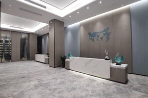 A reception area with a marble floor, a reception desk, and a wall-mounted decorative piece. - Kastin Hotel (Shantou)