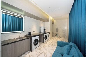 Habitación de hotel moderna con un espejo grande, lavadora integrada, sofá y ventana con cortinas.