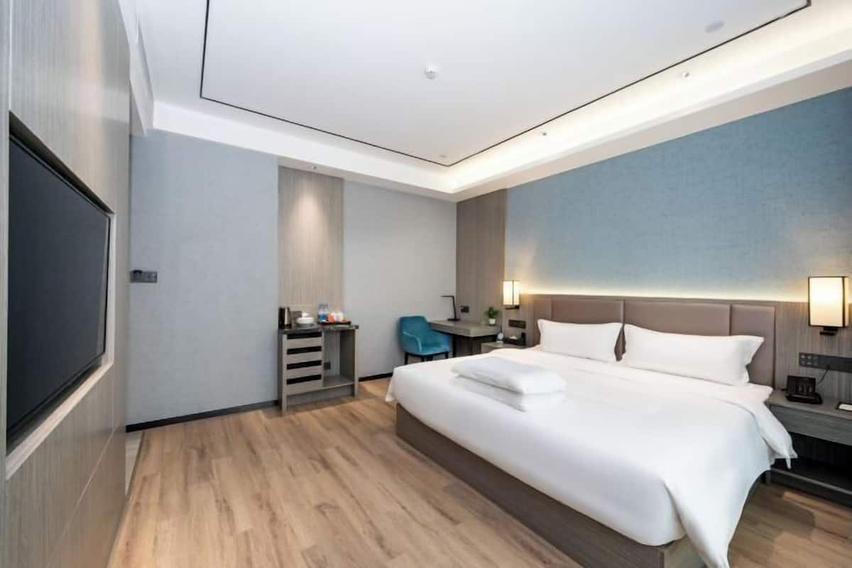A modern hotel room with a large bed, a desk, a chair, and a TV.