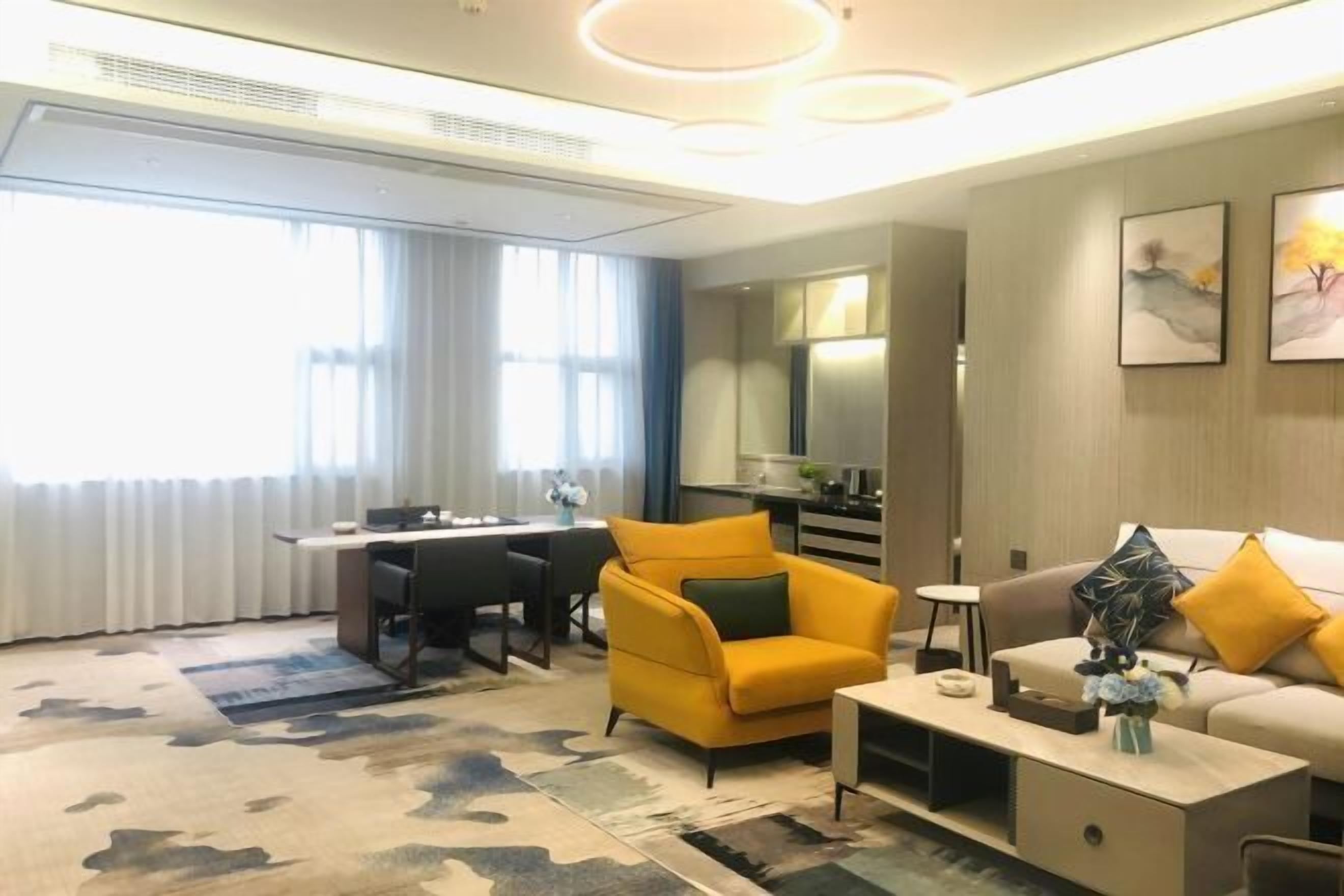 A modern living room with a sofa, armchair, coffee table, and a dining area with a desk and chairs.