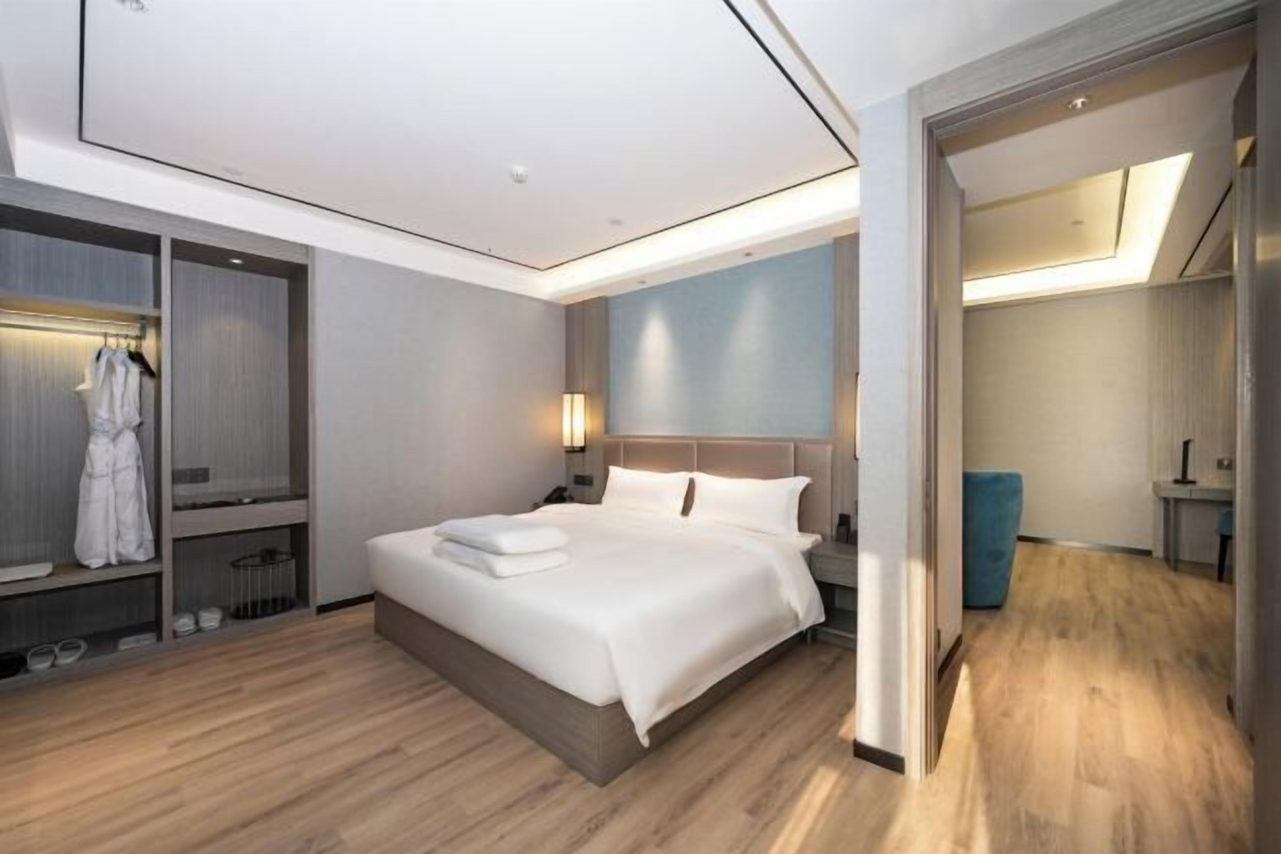 A modern hotel room with a large bed, built-in wardrobe, and a separate seating area.
