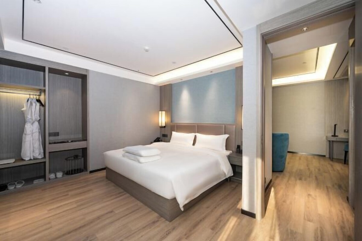 Quarto de hotel moderno com uma cama grande, roupeiro embutido e uma área de estar separada.