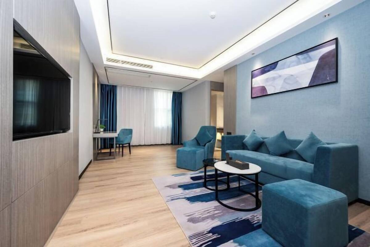 A modern living room with a sofa, chairs, a coffee table, a flat-screen TV, and a painting on the wall.