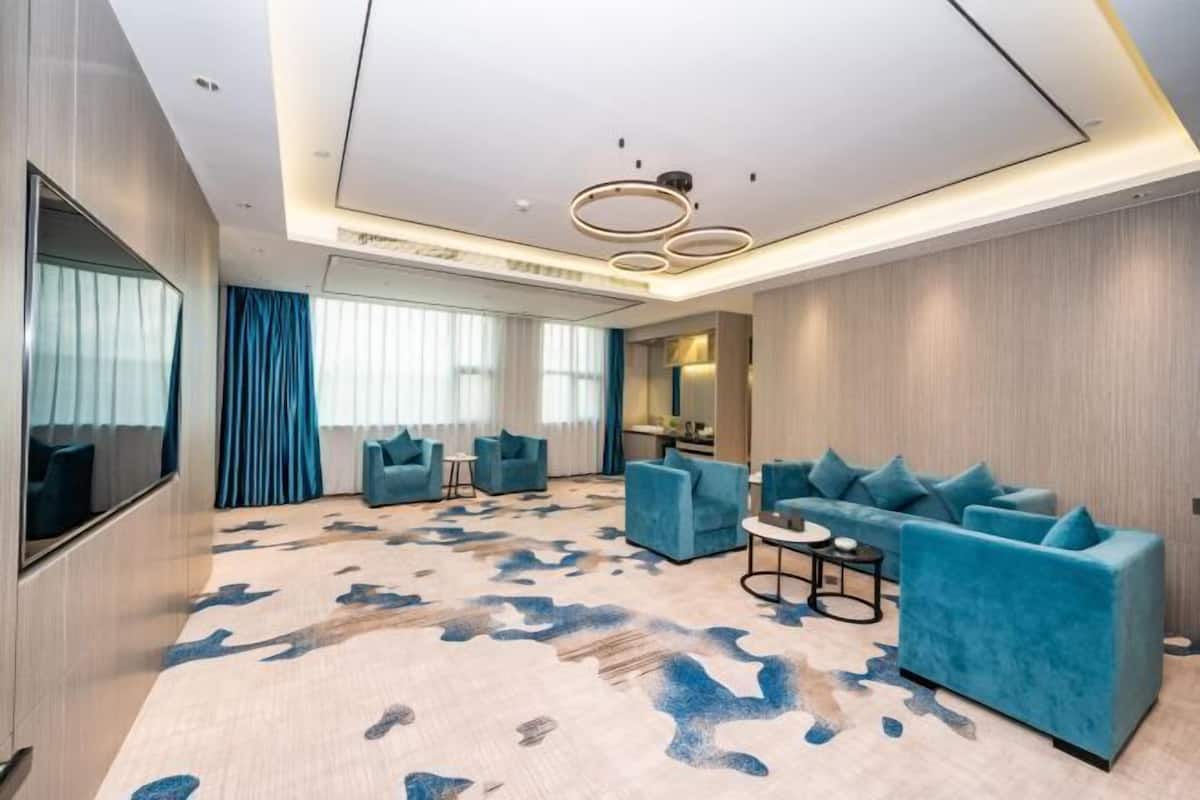 A modern hotel room with a large sofa, two armchairs, a coffee table, and a TV.