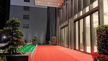 Un pasillo de hotel con alfombra roja, plantas en macetas y fachada de edificio moderna.