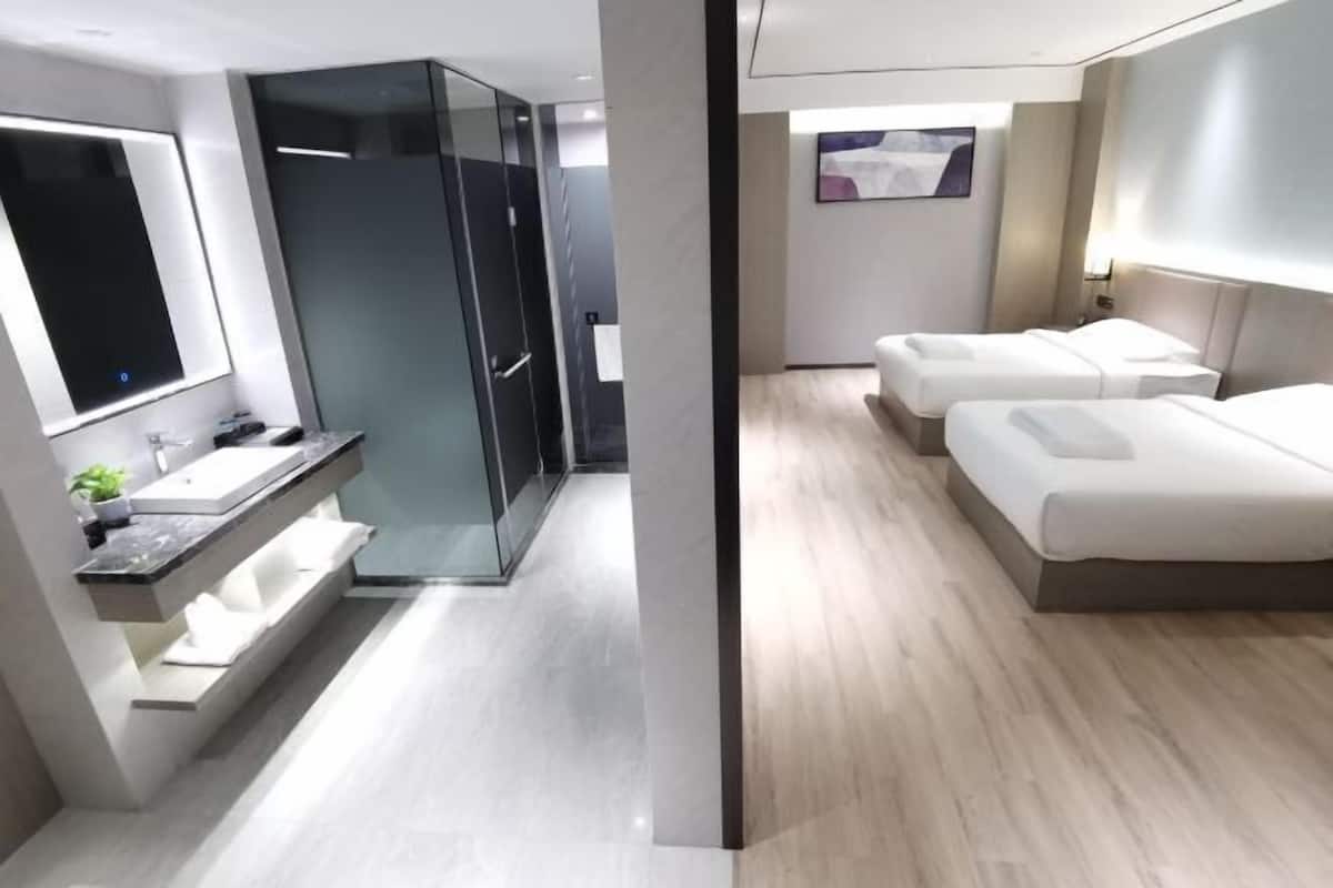 A modern hotel room with a glass-enclosed shower, a vanity with a mirror, and two beds.