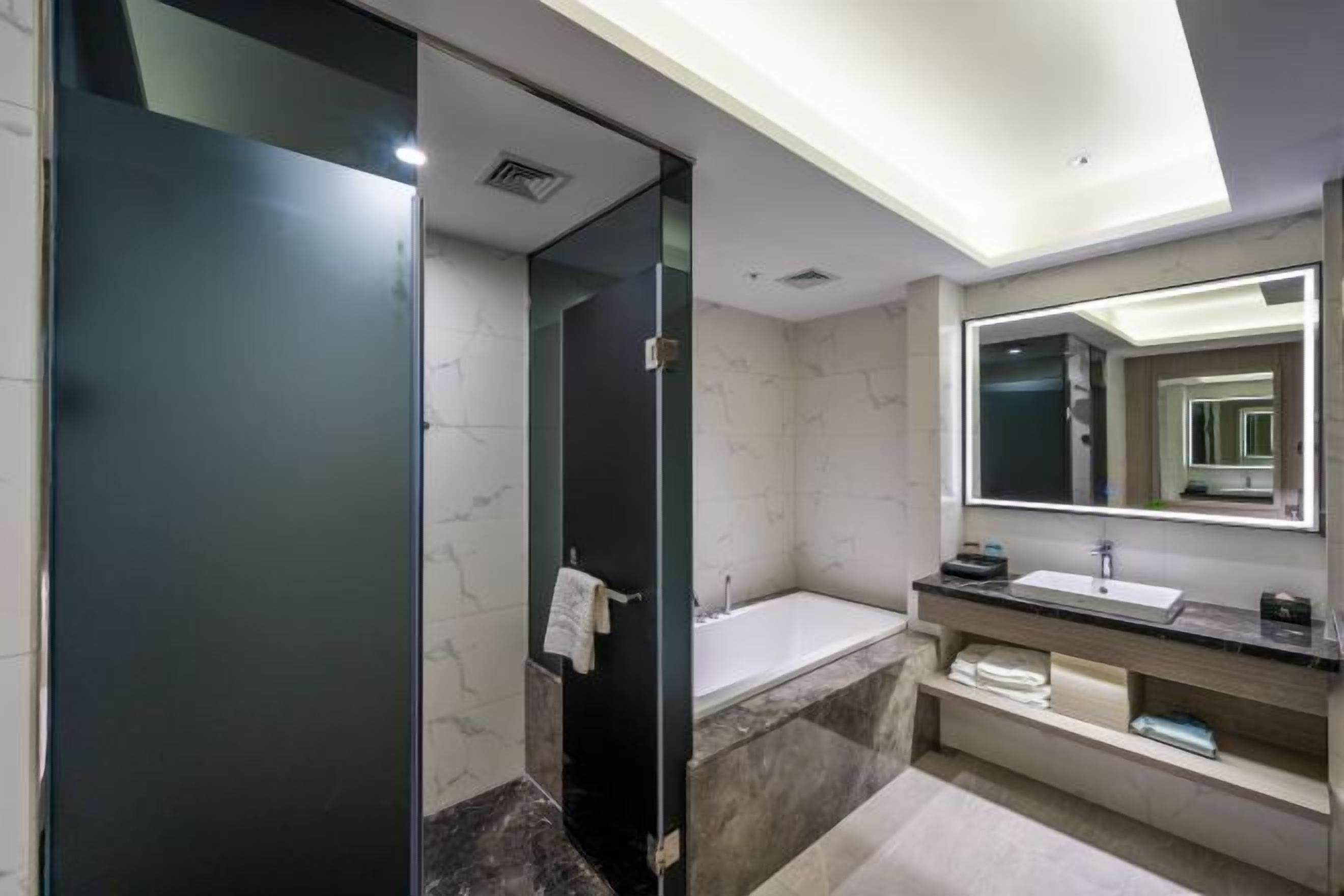 Un baño moderno con cabina de ducha de vidrio, una bañera independiente, un espejo grande y un tocador con azulejos de mármol.