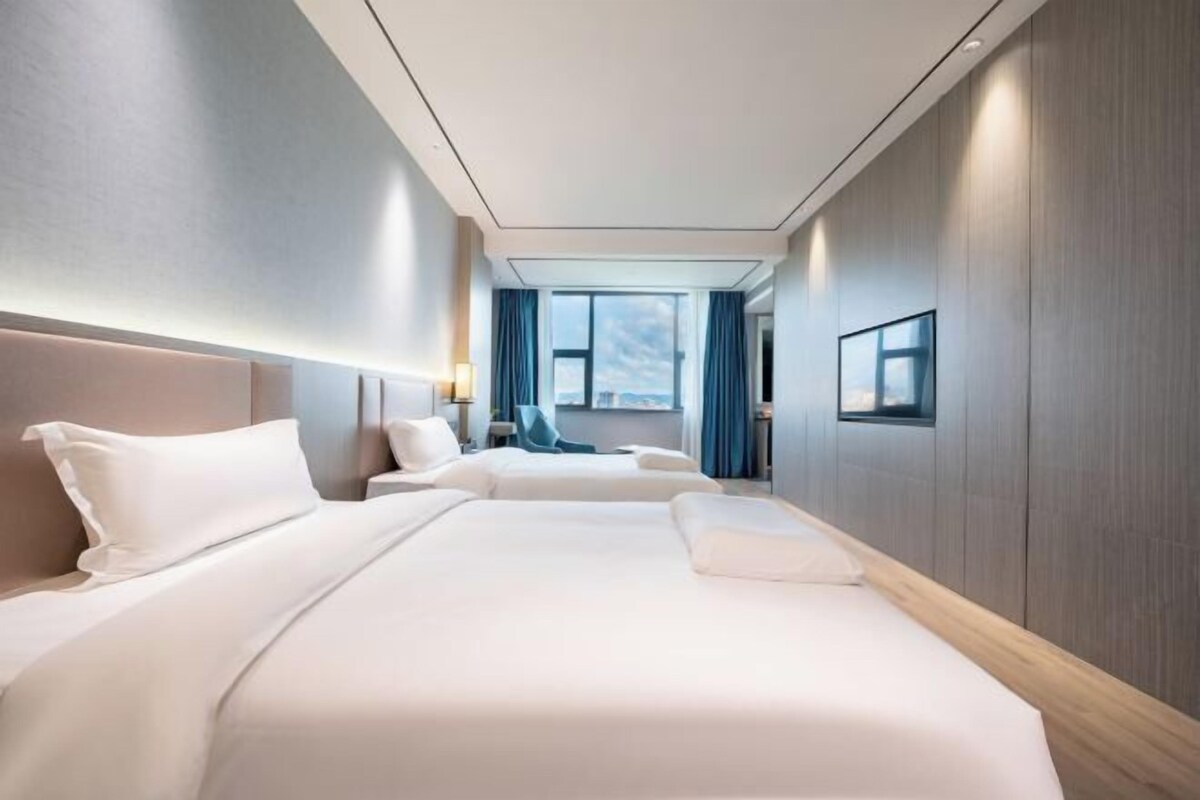 Quarto de hotel com duas camas, uma janela grande, vista da cidade e design moderno.