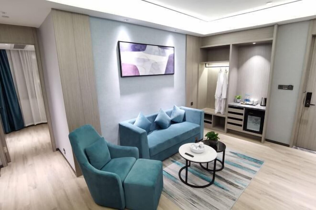 Uma sala de estar moderna com um sofá, poltrona e mesa de centro. Há um quadro na parede e uma pequena planta na mesa.