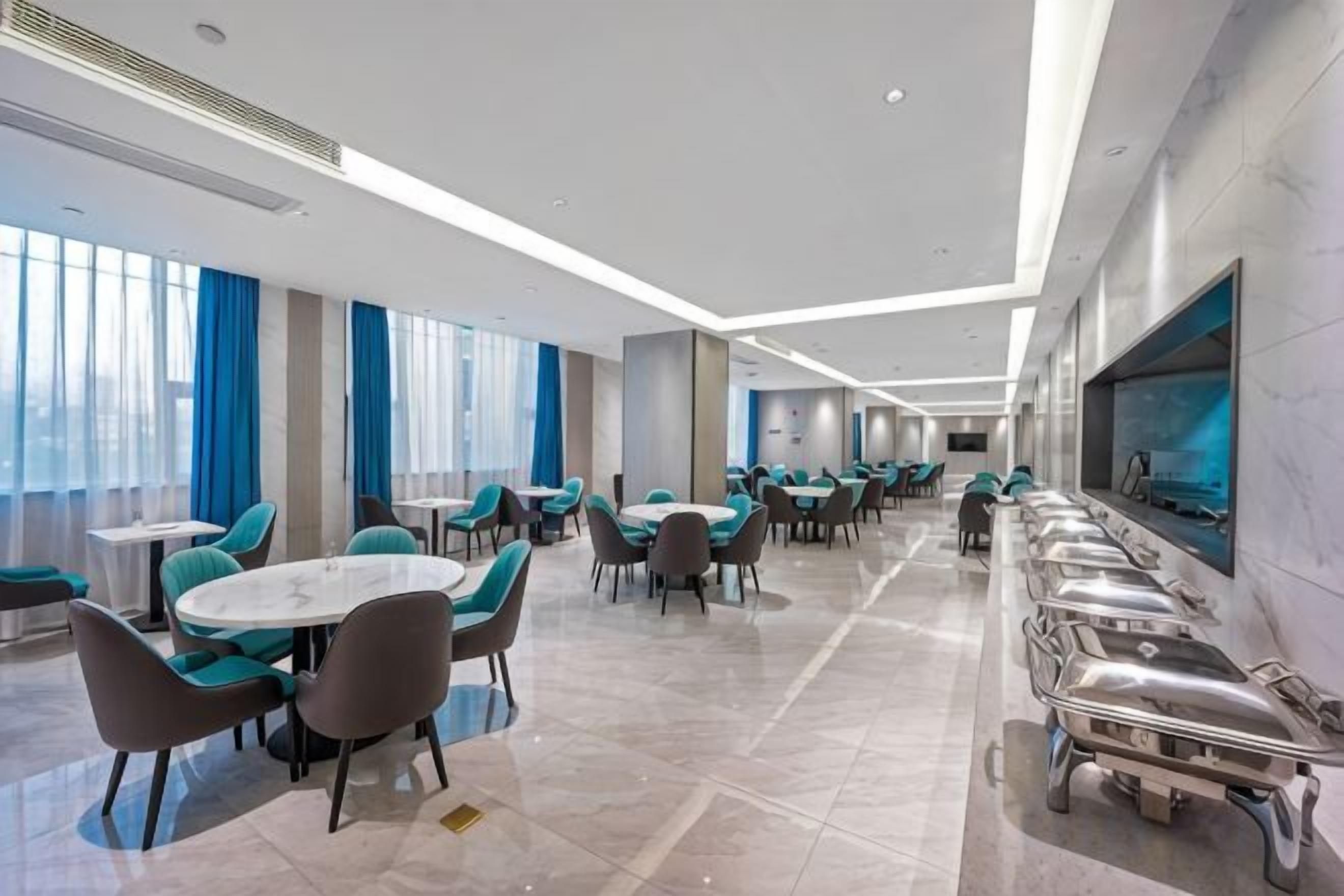 A hotel dining area with multiple tables and chairs, a long buffet line, and large windows.