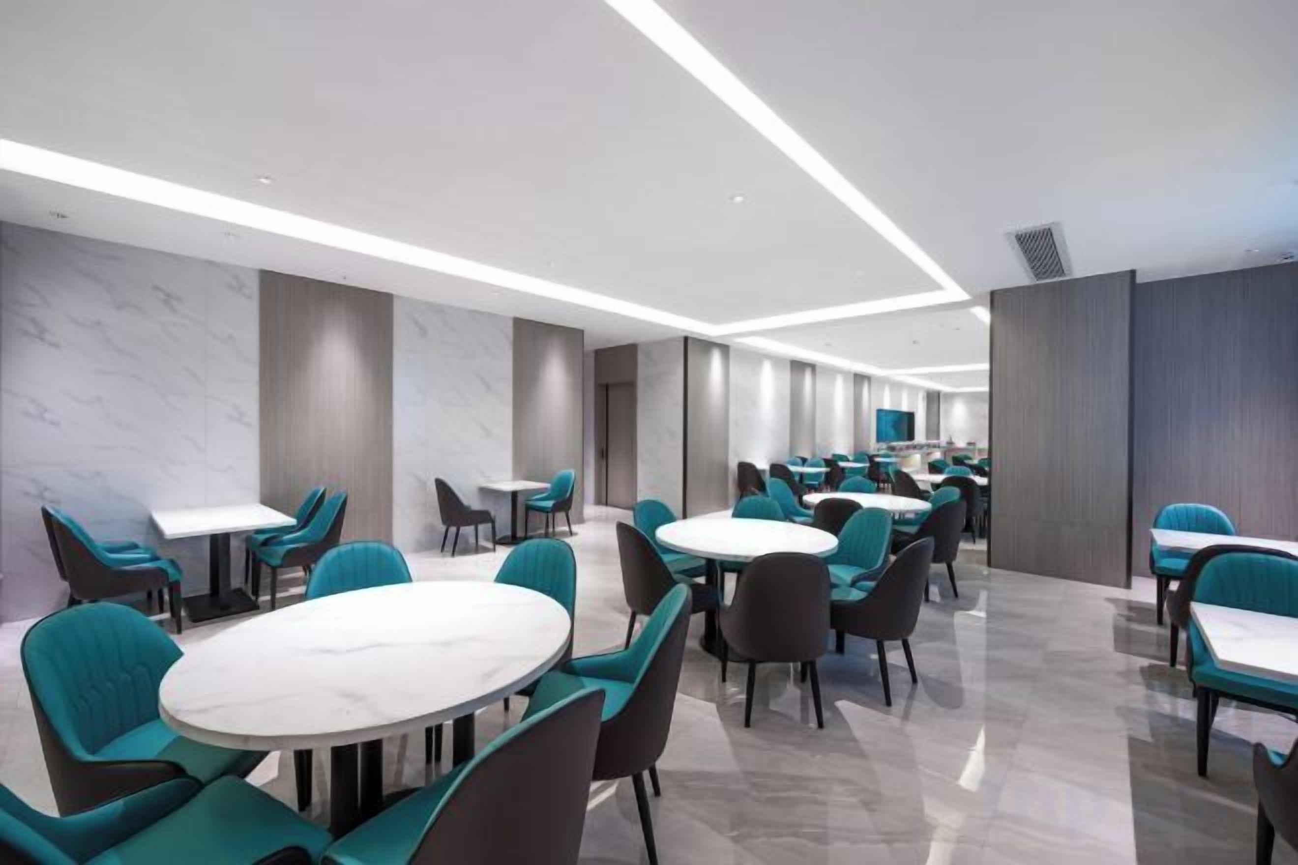 Un área de comedor de hotel moderna con mesas redondas y sillas color turquesa, con un diseño limpio y minimalista.