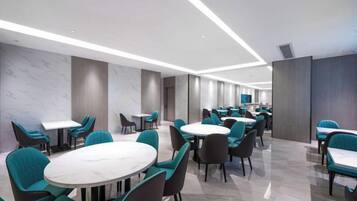 Un área de comedor de hotel moderna con mesas redondas y sillas color turquesa, con un diseño limpio y minimalista.