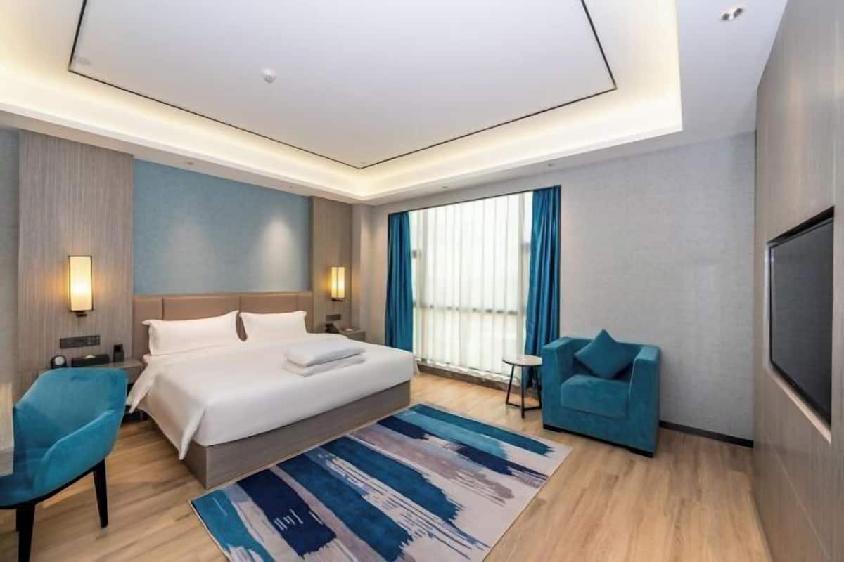 A modern hotel room with a large bed, a sofa, a TV, and a window with curtains.