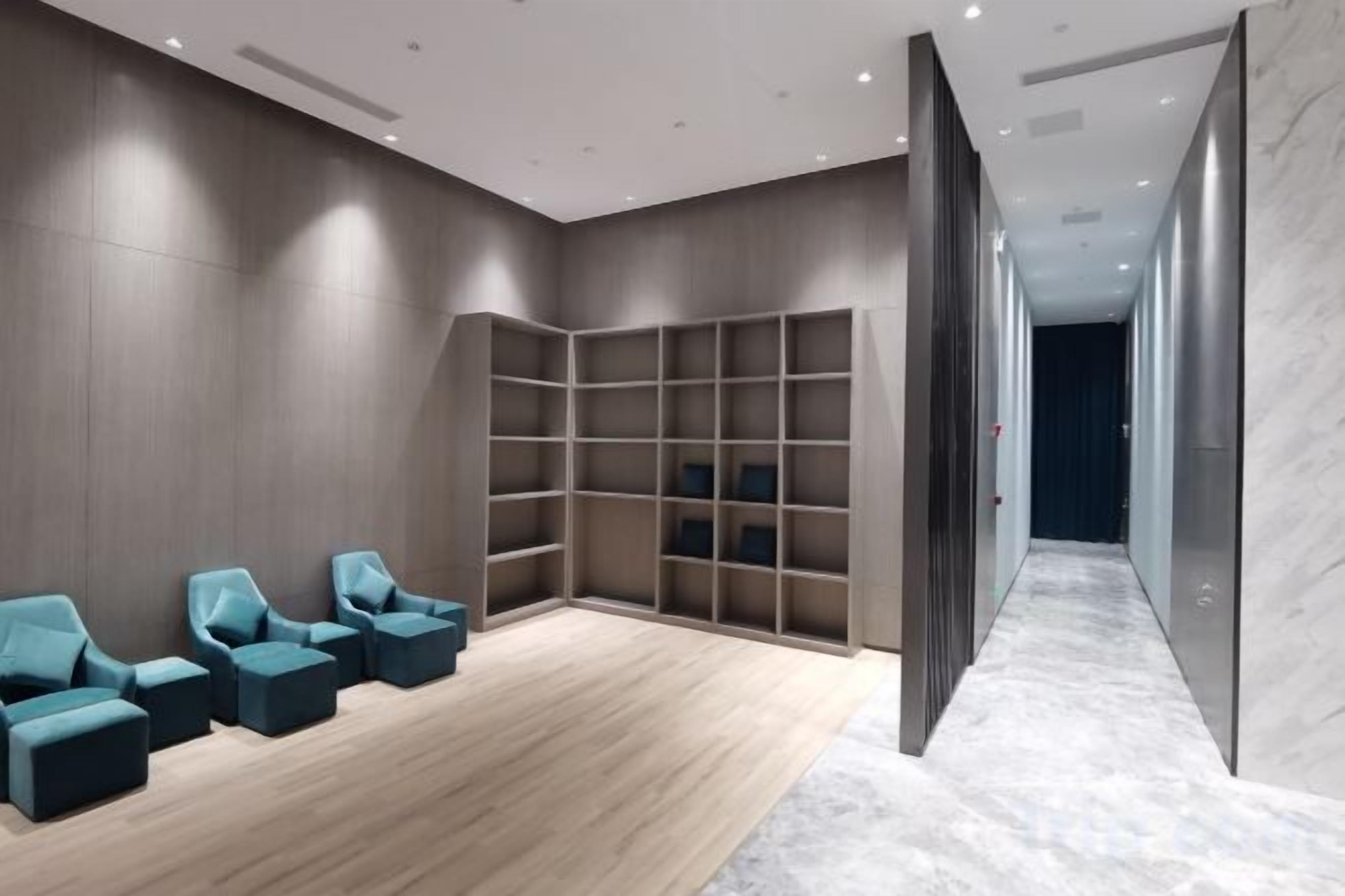 A modern hotel lobby with a seating area, a large bookshelf, and a marble floor.