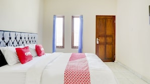 A bedroom with a bed, two windows with curtains, a wooden door, and a headboard. - Hotel O Pondok Dukuh (Nusa Dua)