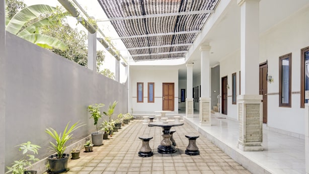 A courtyard with a tiled floor, potted plants, a round table with chairs, and a covered area with a patterned roof. - Hotel O Pondok Dukuh (Nusa Dua)