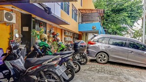 A row of parked motorcycles and a car outside a building with a blue and yellow facade.