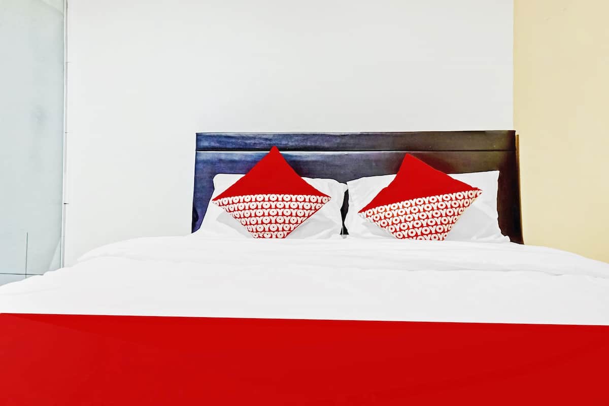 Cama com roupa de cama branca e duas almofadas vermelhas com padrão repetido.