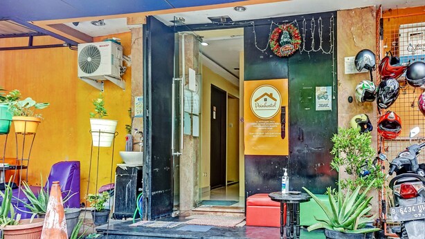 A hostel entrance with a signboard, potted plants, and helmets on display.