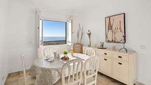 Un comedor con una mesa dispuesta para dos, vista al mar y un aparador con adornos.
