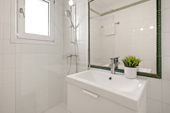 Une salle de bain moderne avec un lavabo blanc, une douchette à main et une plante en pot.