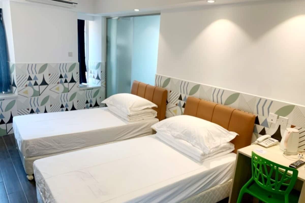 Une chambre d’hôtel avec deux lits, un fauteuil vert et une petite table sur laquelle se trouvent un téléphone et une machine à café.
