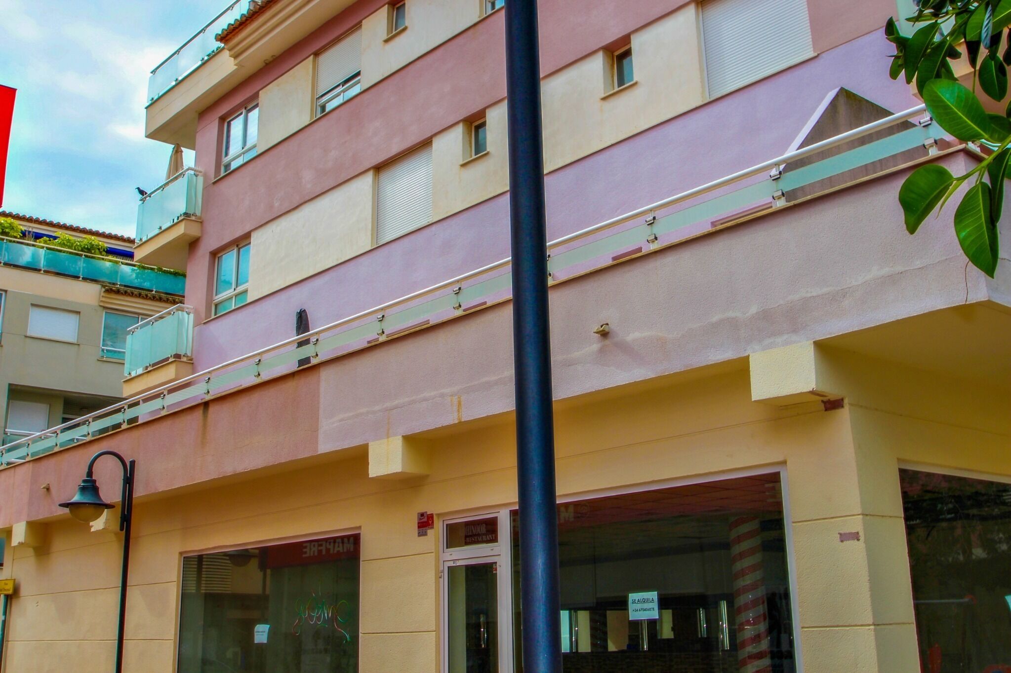 Un immeuble à plusieurs étages doté de balcons, avec un commerce visible au rez-de-chaussée et un lampadaire dans la rue.