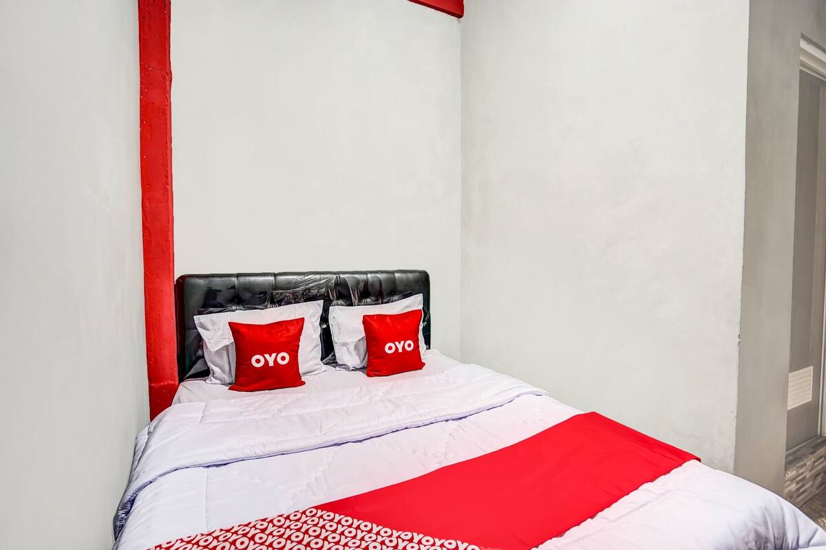 Een bed met een zwart hoofdeinde, witte beddengoed en rode accenten.