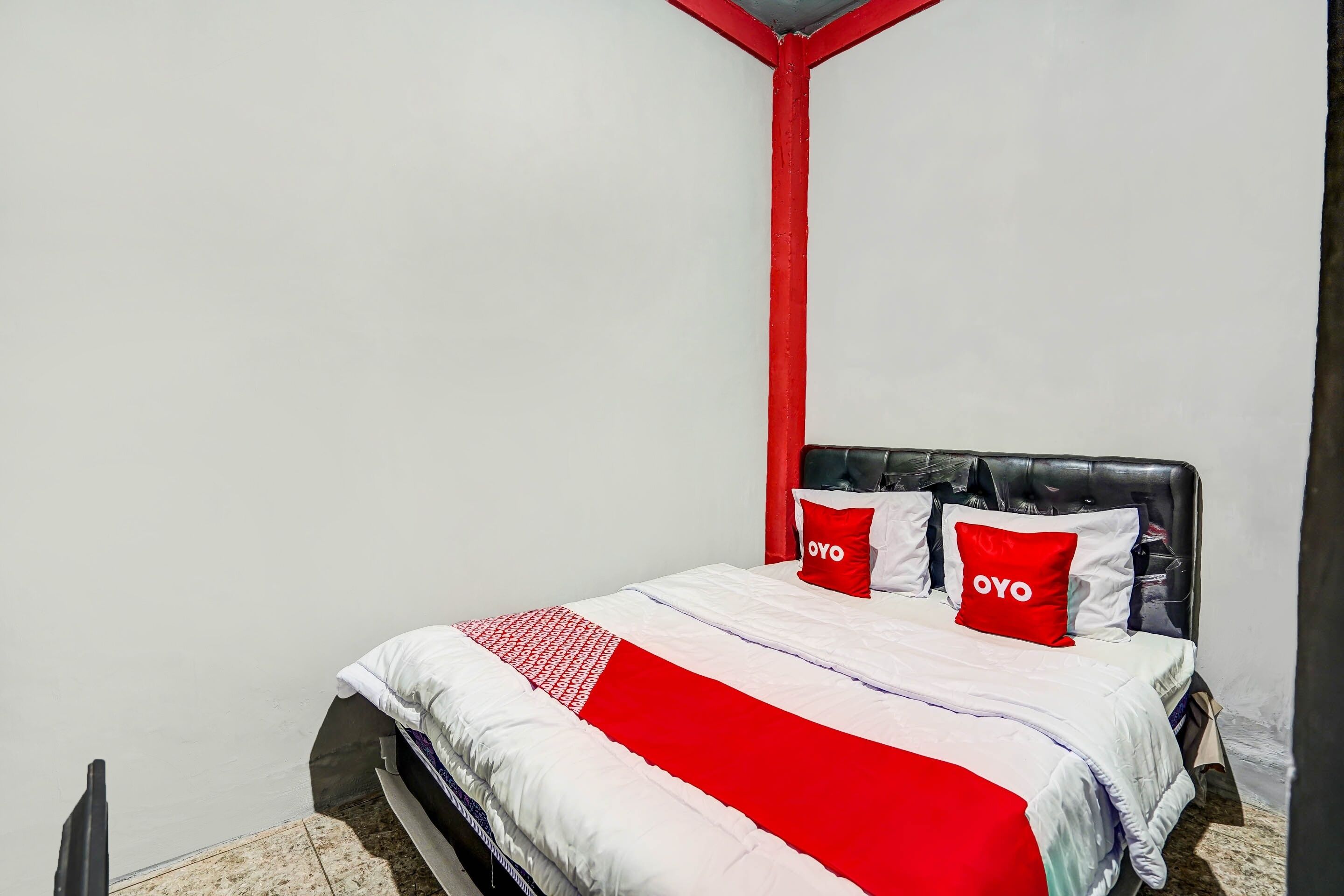 Una cama con una colcha roja y blanca, dos almohadas rojas con la palabra "OYO" y un cabecero negro.