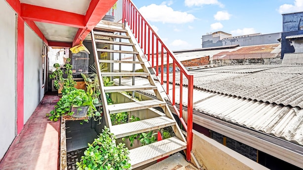 Eine rote Metalltreppe führt zu einem Balkon mit Blumentöpfen.