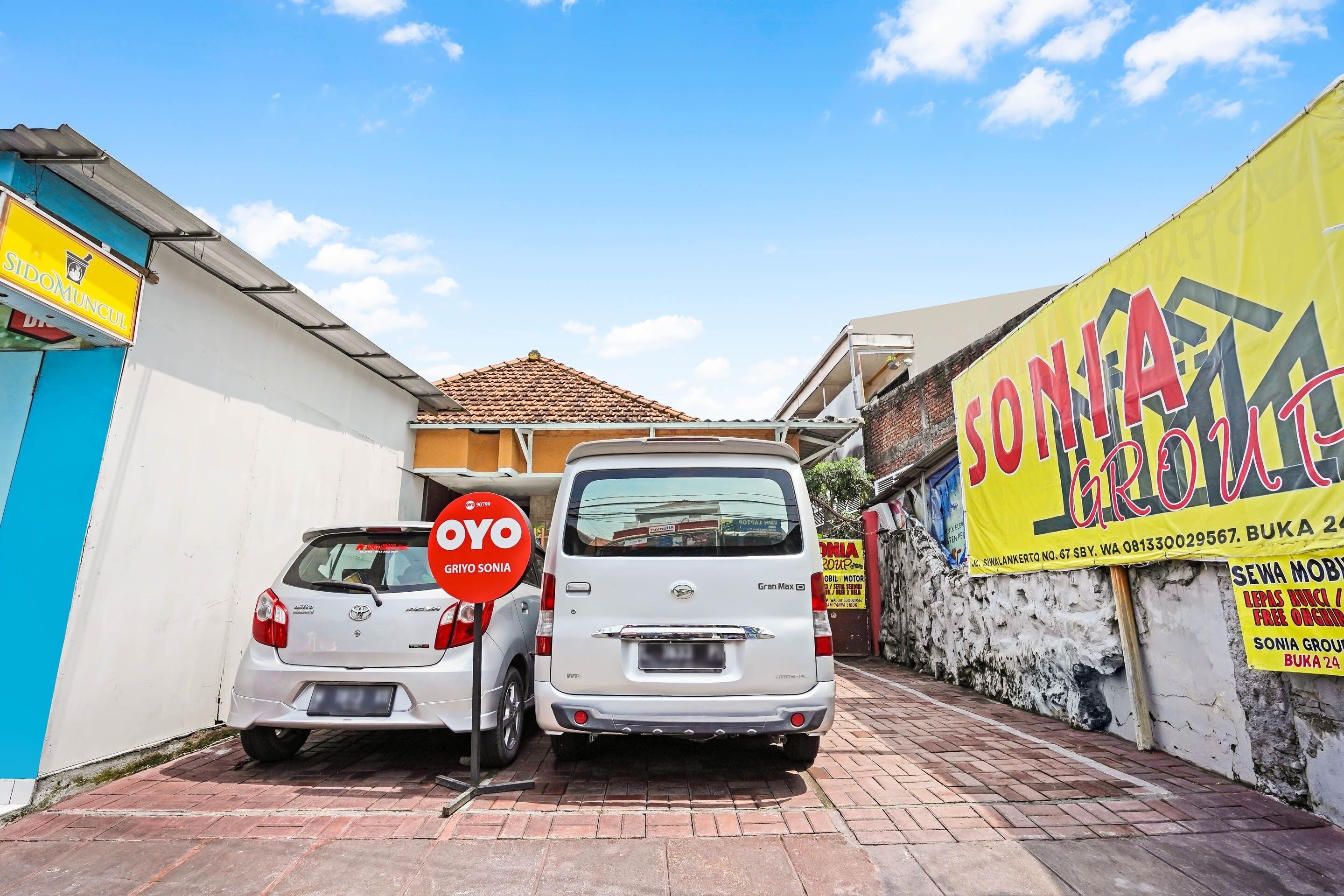 A white van parked in a narrow street with a yellow banner advertising 'SONIA GROUP' and a sign for 'SIDOMUNCUL'.