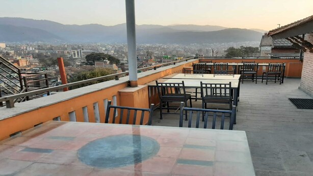 Eine Dachterrasse mit Tischen und Stühlen, die einen Blick auf eine Stadt und entfernte Berge bietet.
