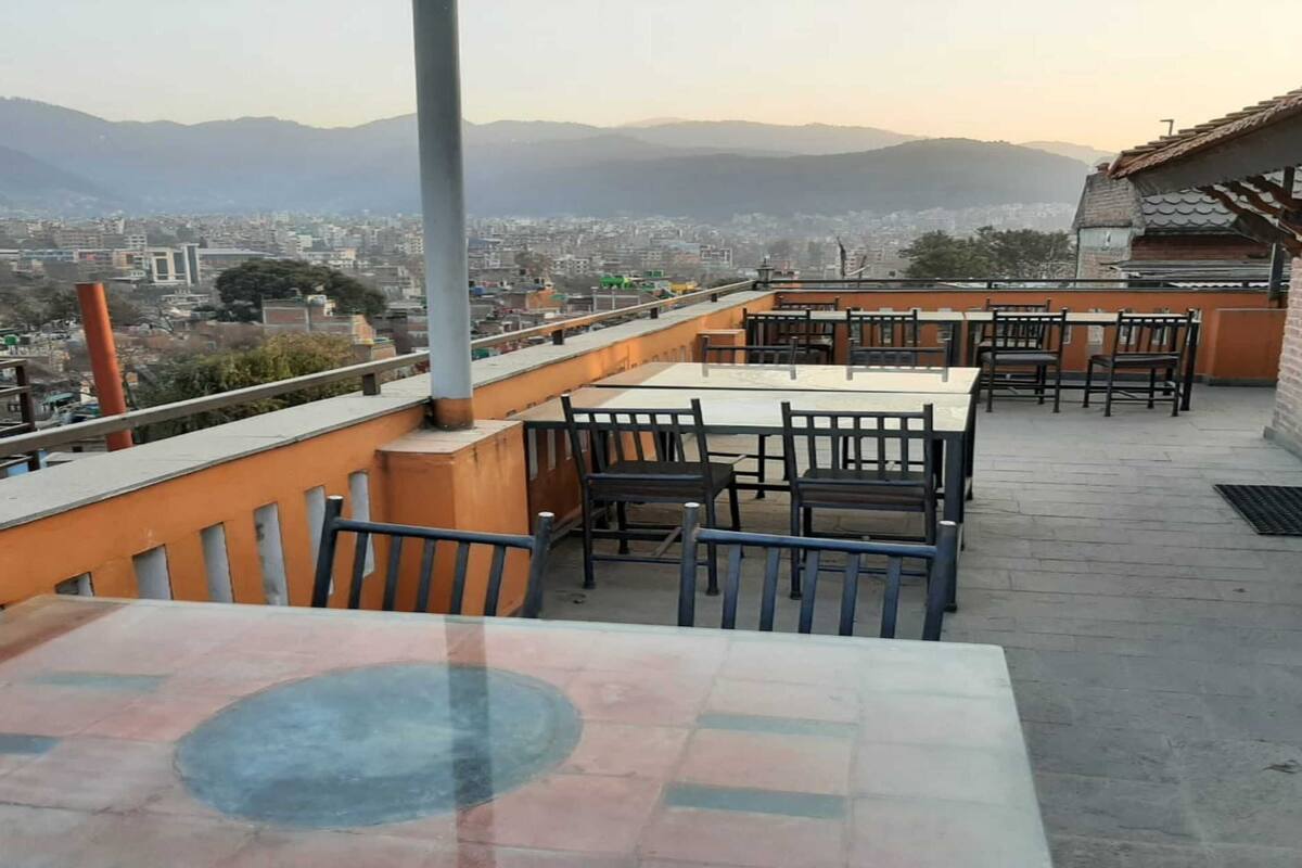 Une terrasse sur le toit, aménagée avec des tables et des chaises, d’où l’on peut admirer une vue sur la ville et les montagnes au loin.