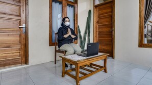 Iemand zit aan een houten tafel met een laptop, in een kamer met houten deuren en een cactus.