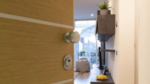 Interior moderno com porta de madeira, pequena área de estar com um bean bag e vista para a paisagem urbana através de uma janela grande.