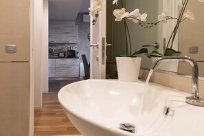 Une salle de bain avec un lavabo blanc, un miroir et une orchidée en pot.